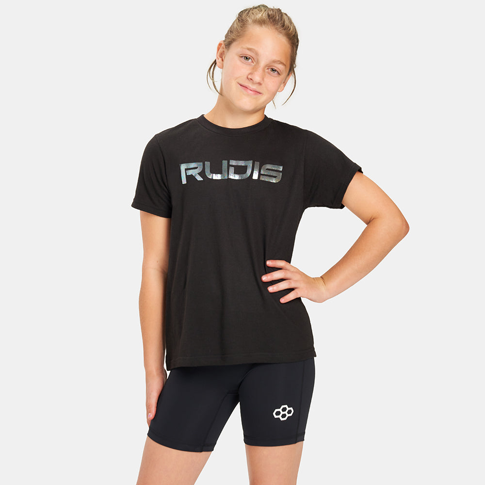 A young girl stands confidently in a black t-shirt with RUDIS printed on it paired with black shorts featuring a logo showcasing a casual athletic look