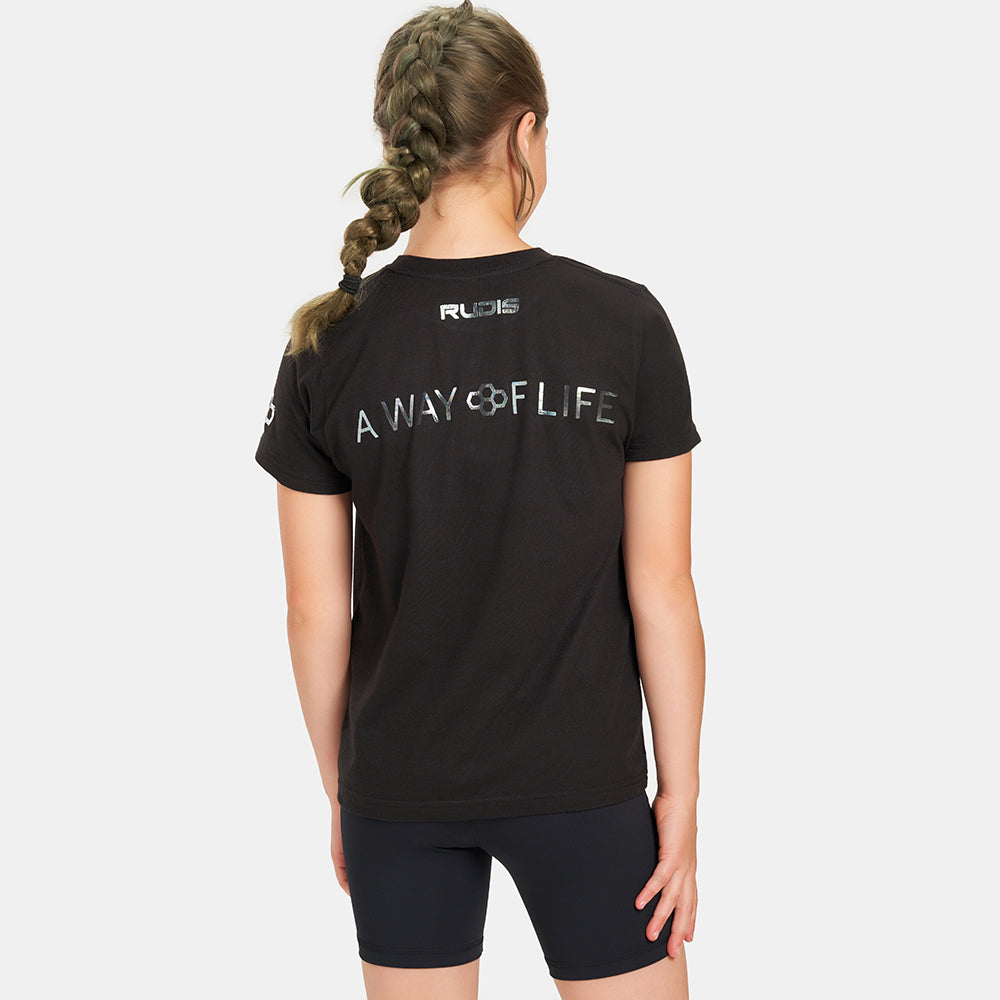 A young girl wearing a black T-shirt with the phrase A WAY OF LIFE printed on the back paired with black shorts showcasing a sporty and casual style