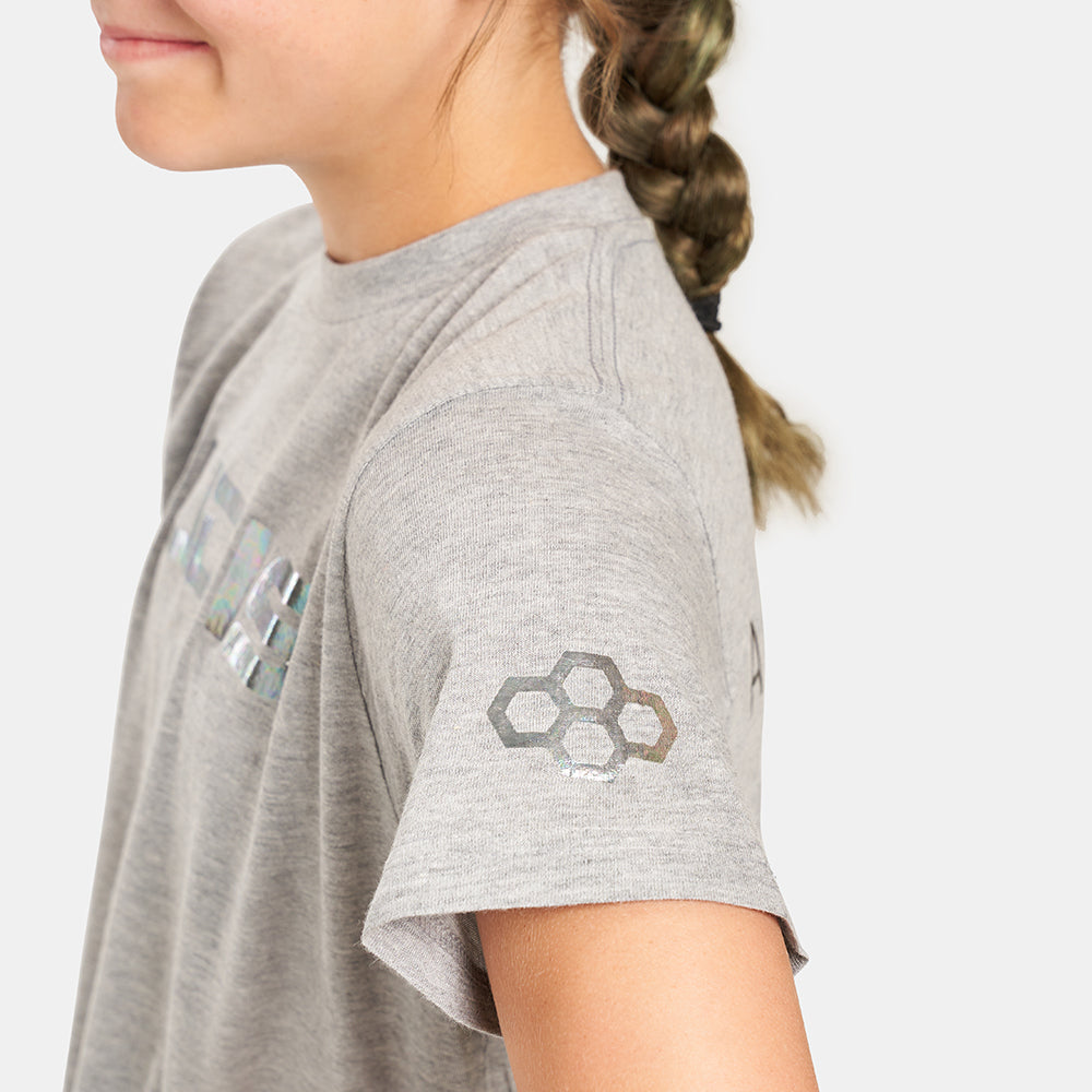 A young girl wearing a gray short-sleeved t-shirt with a shiny logo and a patterned design on the sleeve