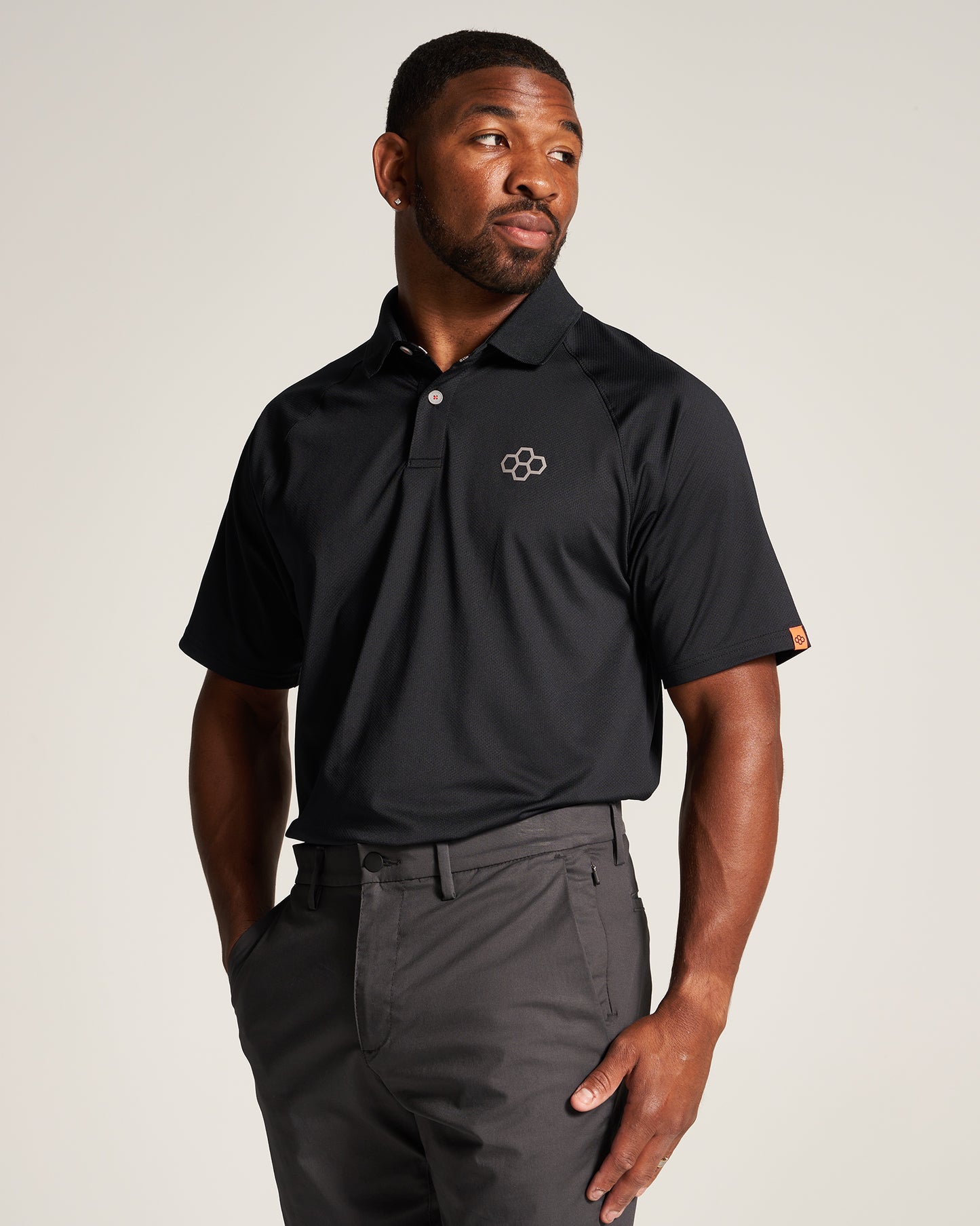 A man wearing a black athletic polo shirt and gray trousers posing with a confident expression against a neutral background