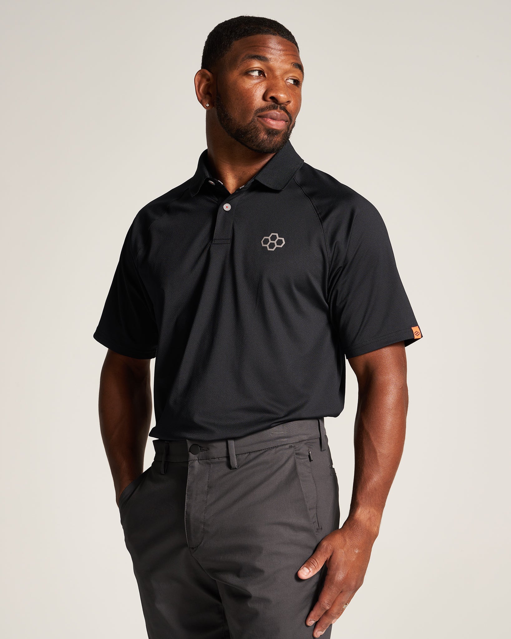 A man wearing a black athletic polo shirt and gray trousers posing with a confident expression against a neutral background