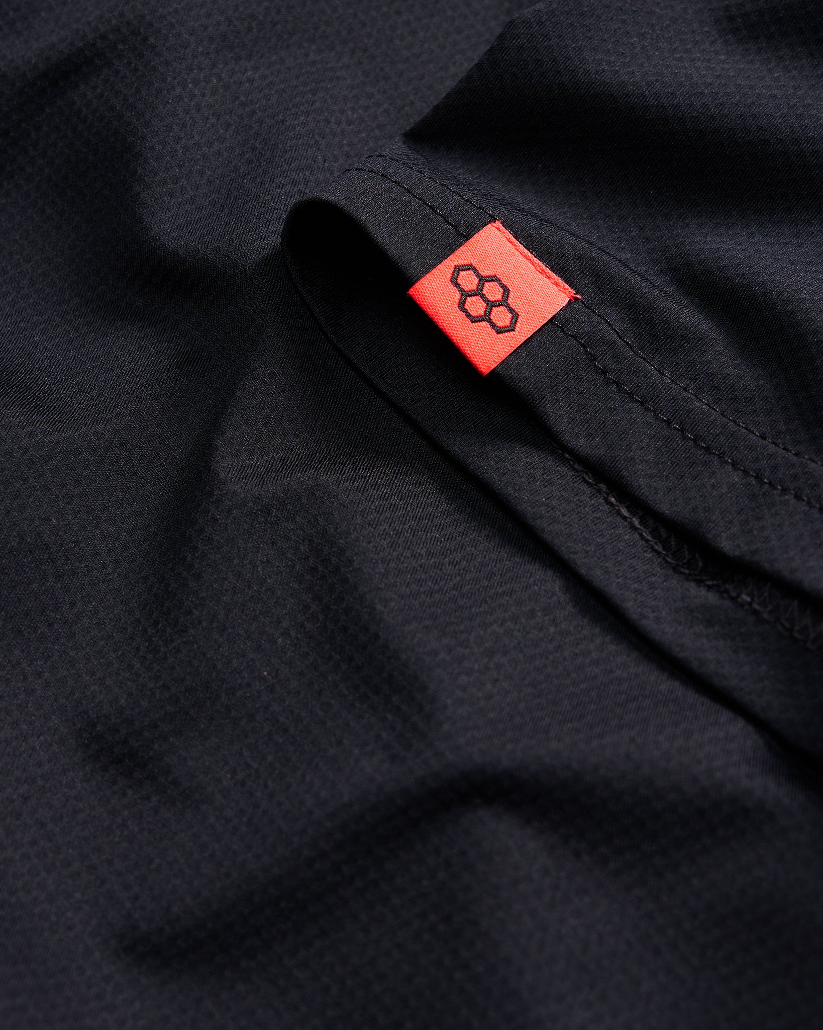 A close-up of a black fabric showcasing a textured surface with a bright red tag featuring a logo on the edge