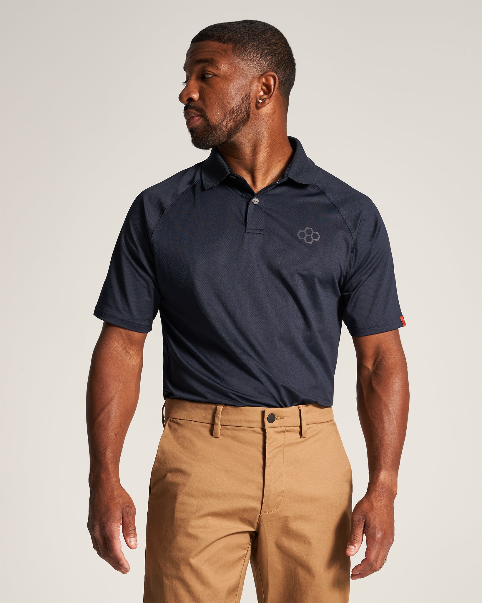 A man in a navy polo shirt and khaki pants poses confidently showcasing a modern casual outfit suitable for various occasions