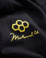 A close-up view of a black fabric showcasing a golden logo featuring interconnected hexagons and the signature of Muhammad Ali