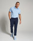 A stylish man is confidently walking in a light blue polo shirt dark pants and light blue sneakers posing against a neutral background