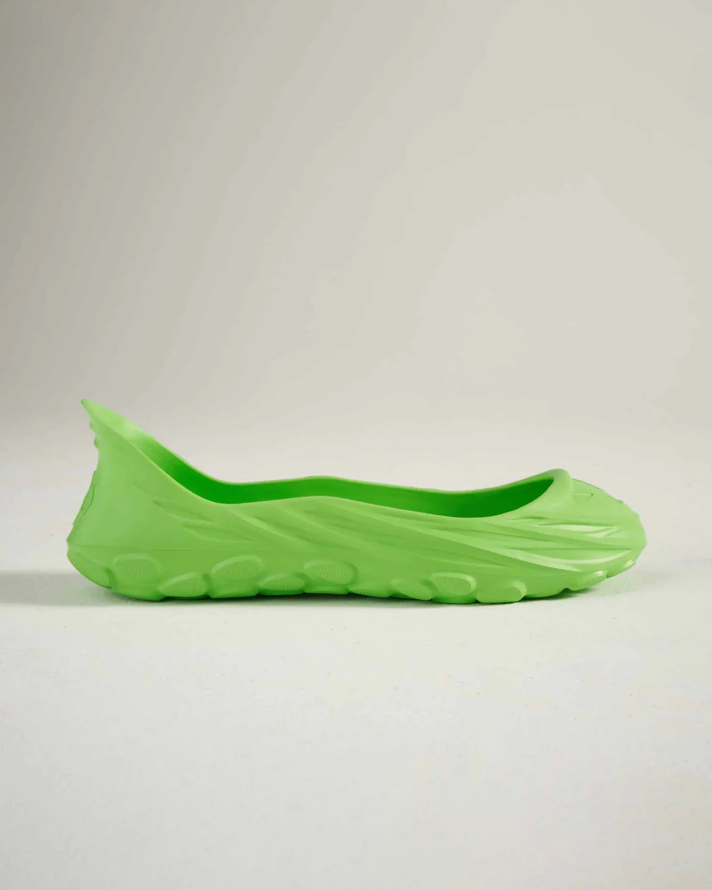 A vibrant green slip-on shoe with a unique design featuring a smooth exterior and textured sole for grip
