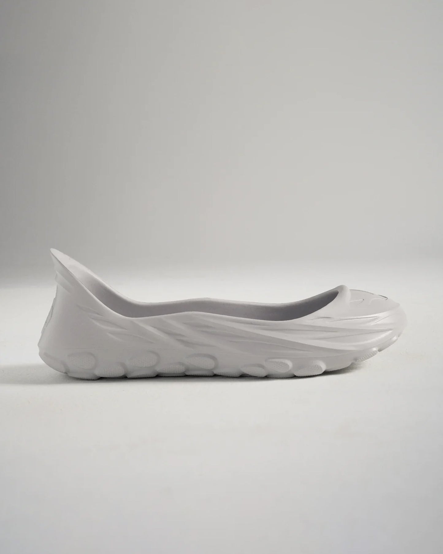 A minimalist gray slip-on shoe with a unique contoured design and textured sole exemplifying modern footwear aesthetics