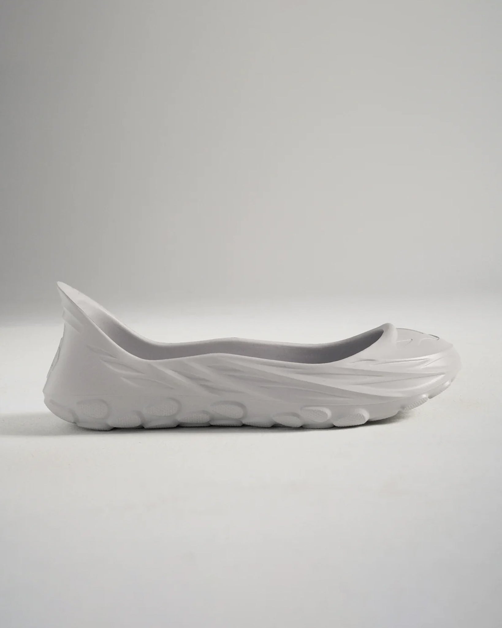 A minimalist gray slip-on shoe with a unique contoured design and textured sole exemplifying modern footwear aesthetics