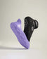 This image displays a pair of athletic shoes known for their innovative design featuring a sleek black upper and a distinctive purple sole with a textured surface for improved grip