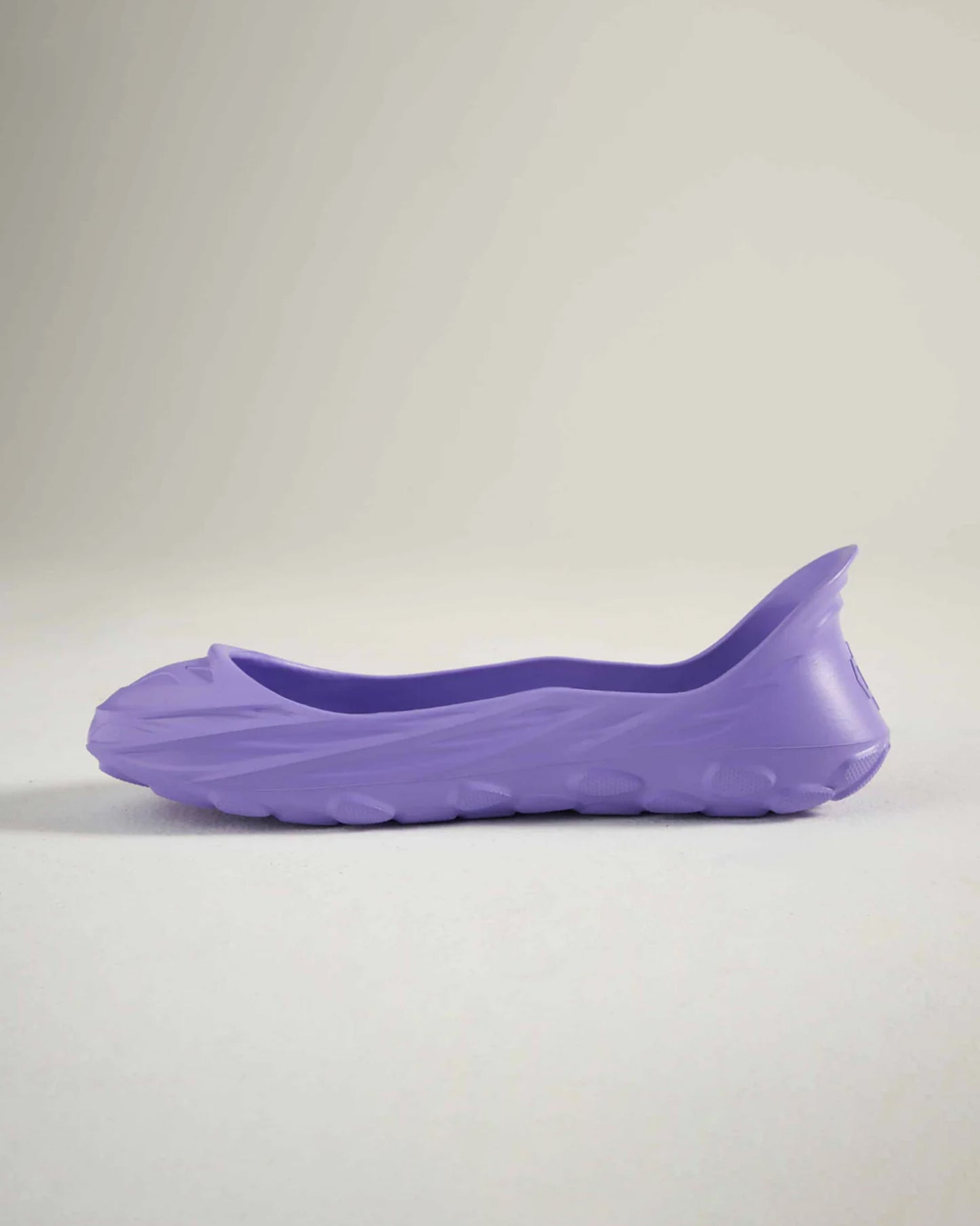 A side view of a sleek purple rubber shoe featuring a minimalist design and textured sole for grip