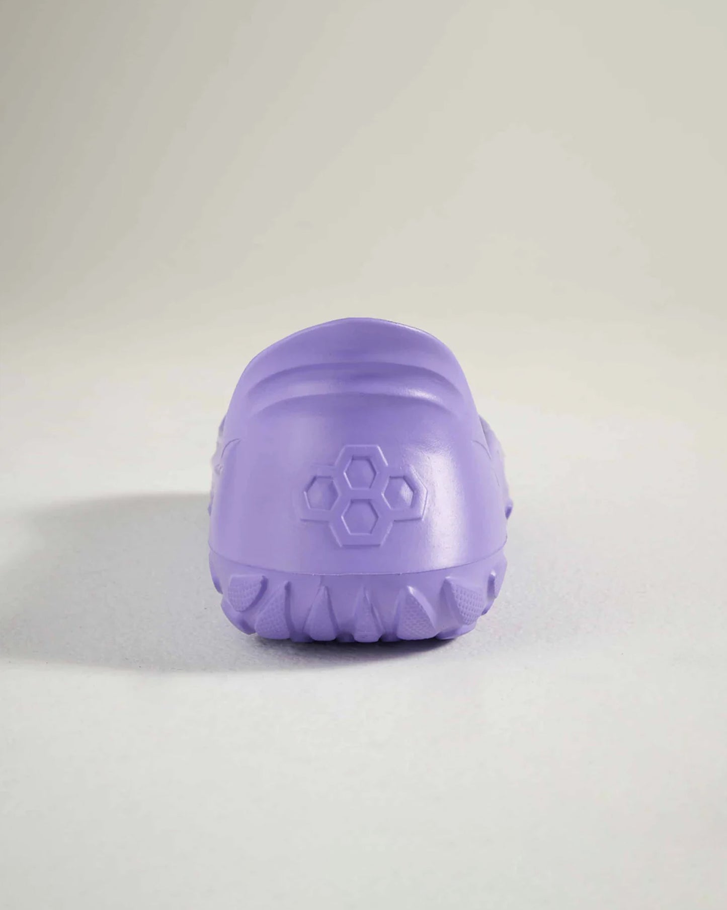 A rear view of a lavender-colored shoe featuring a textured sole and a hexagonal logo on the heel