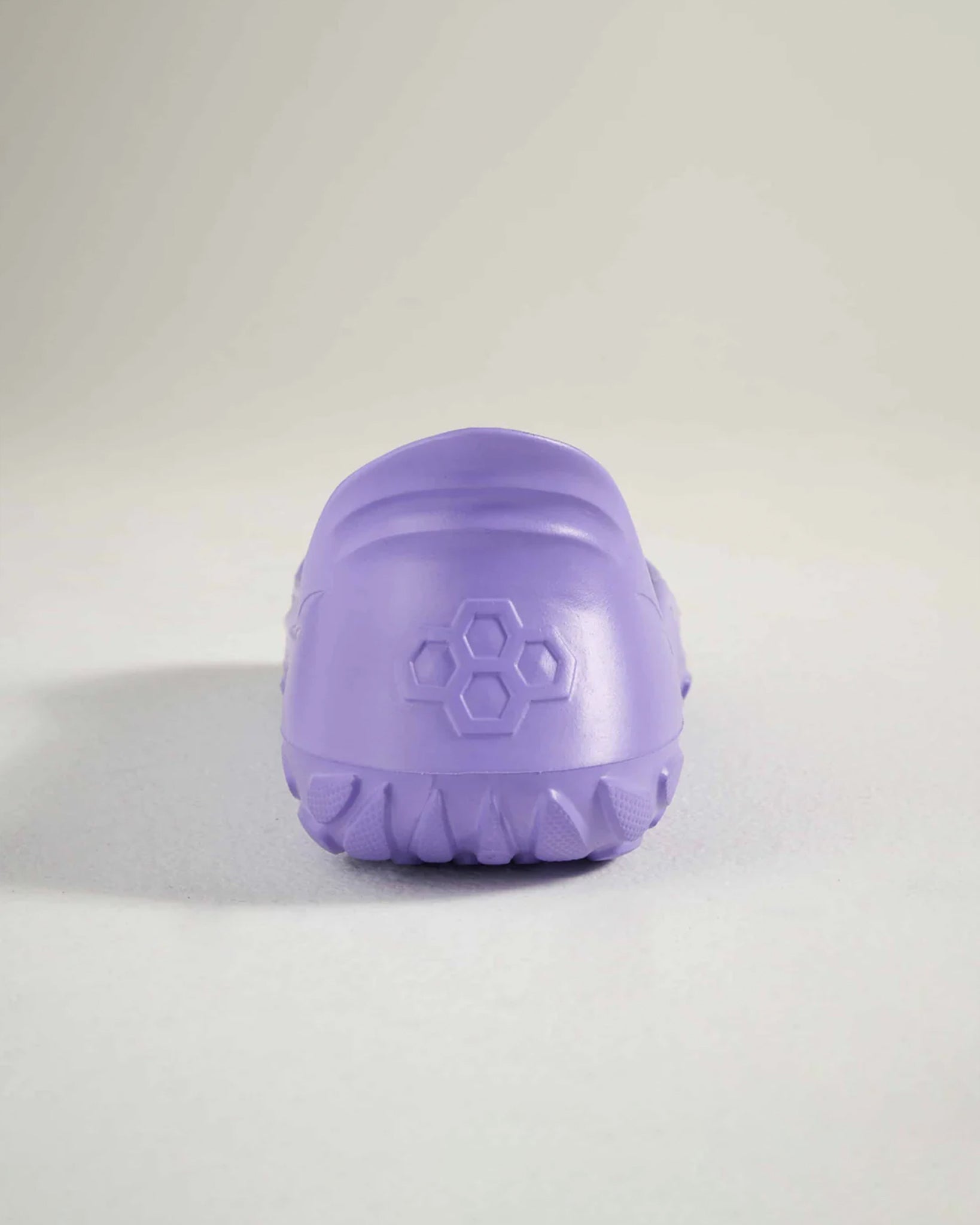 A rear view of a lavender-colored shoe featuring a textured sole and a hexagonal logo on the heel