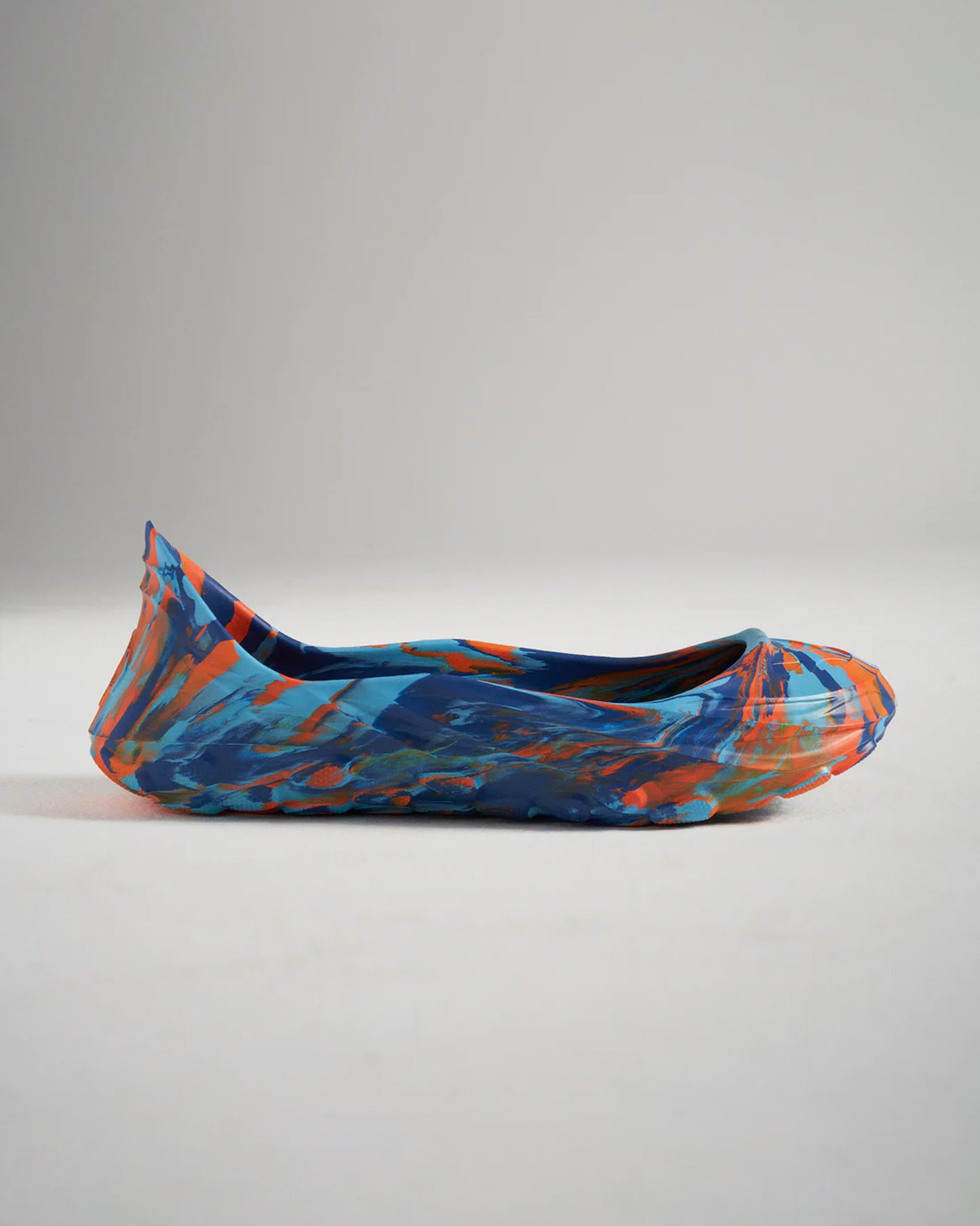 A vibrant and colorful pair of ballet flats showcasing an abstract design in blue orange and teal hues presented in a side view against a neutral background