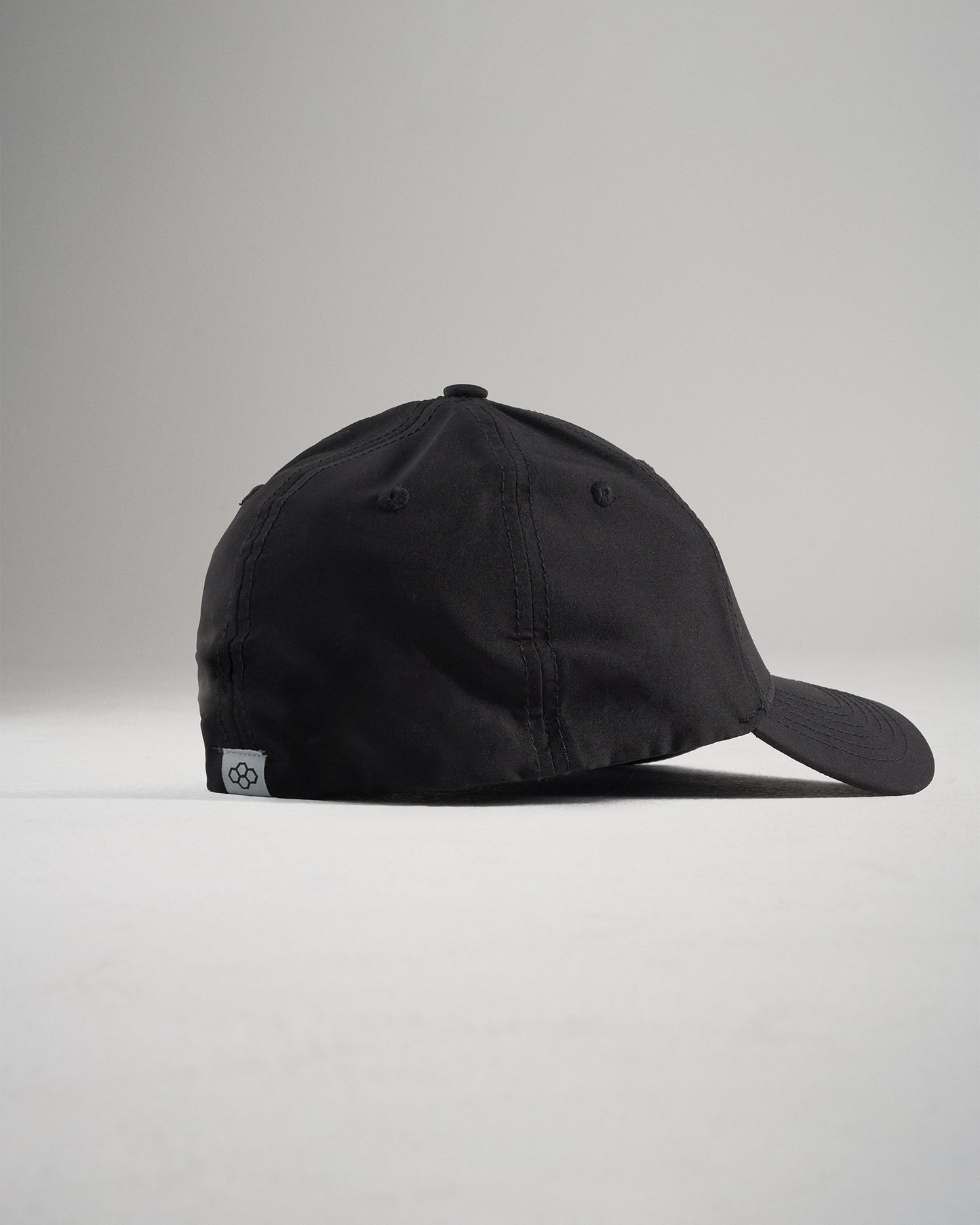 A black baseball cap viewed from the side featuring a curved visor and a signature tag on the back