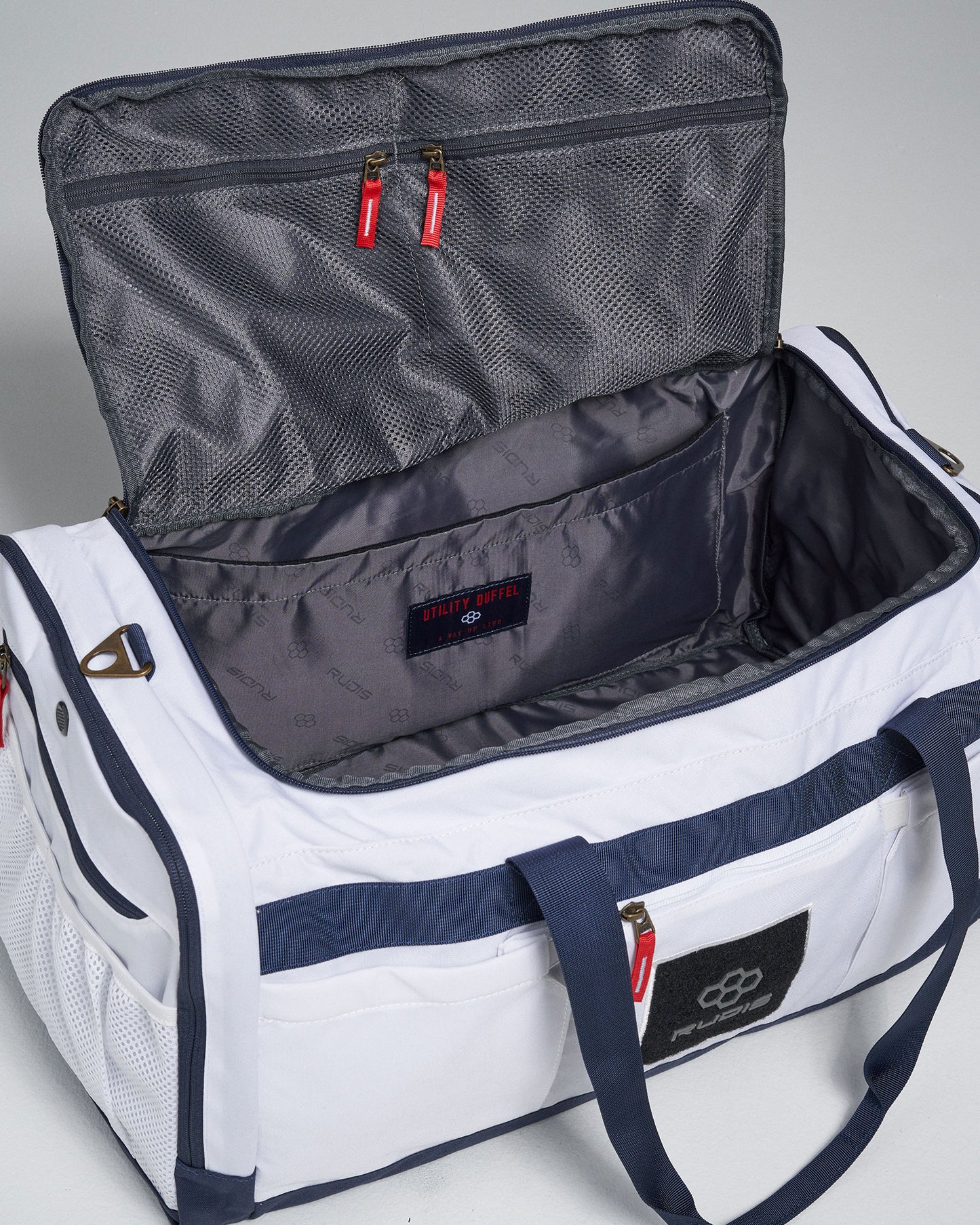A white utility duffel bag with a spacious interior and red zip pulls showcasing compartments for organized storage