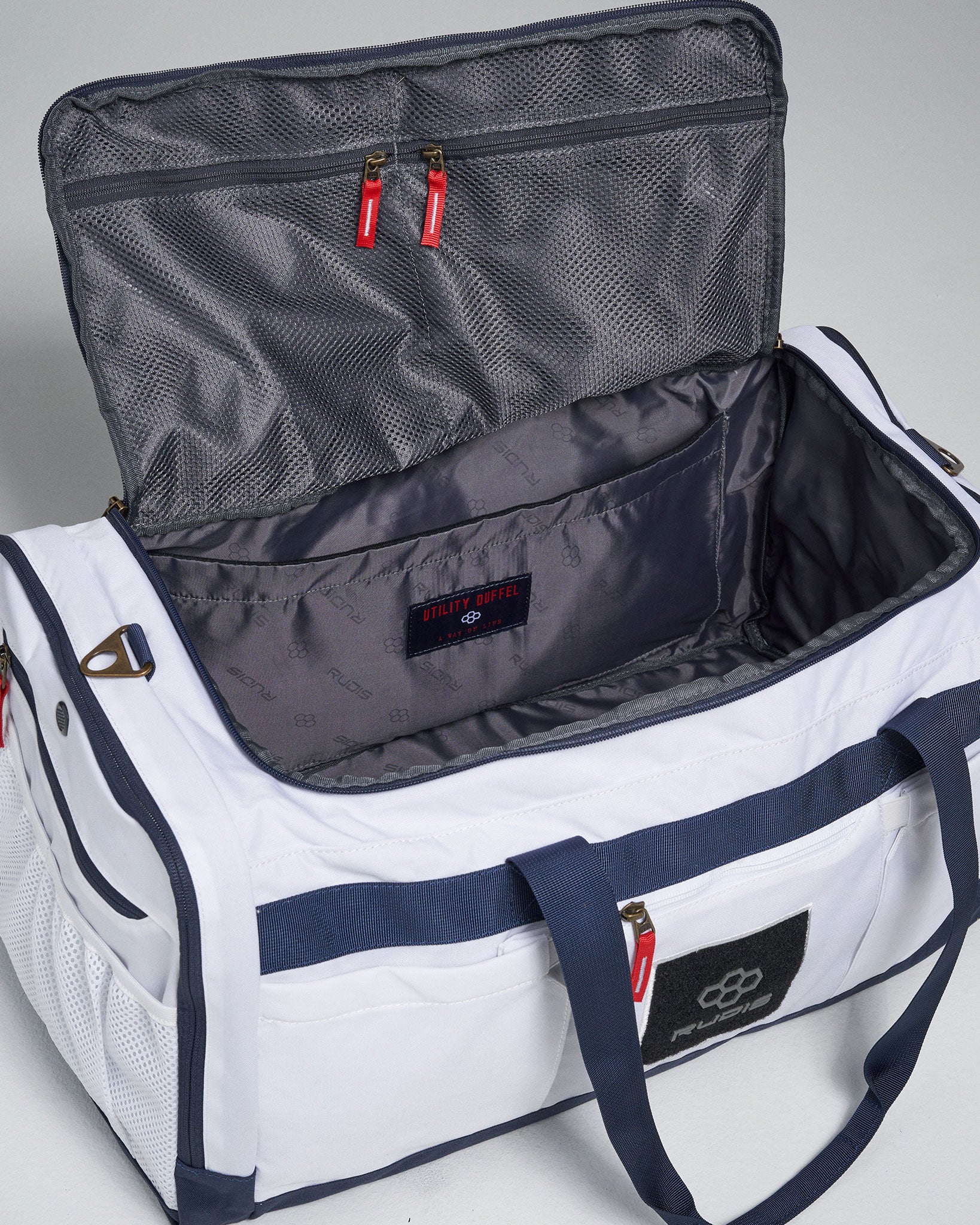 A white utility duffel bag with a spacious interior and red zip pulls showcasing compartments for organized storage