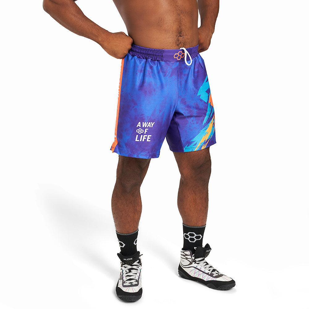 A young man stands confidently wearing vibrant blue and purple swim shorts featuring a bold graphic design along with black and white athletic shoes and socks