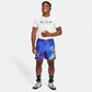 A joyful young man wearing a white T-shirt and colorful purple shorts standing casually with a smile showcasing a fun and sporty style