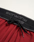 This image displays a close-up view of red athletic shorts featuring a black elastic waistband with the brand name printed on it and contrasting drawstrings for a secure fit