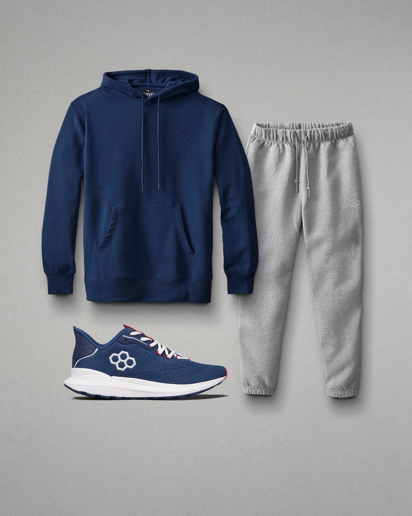 Navy hoodie, gray sweatpants, and blue athletic shoe on a gray background
