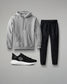 Gray hoodie, black pants, and black sneakers on a gray background