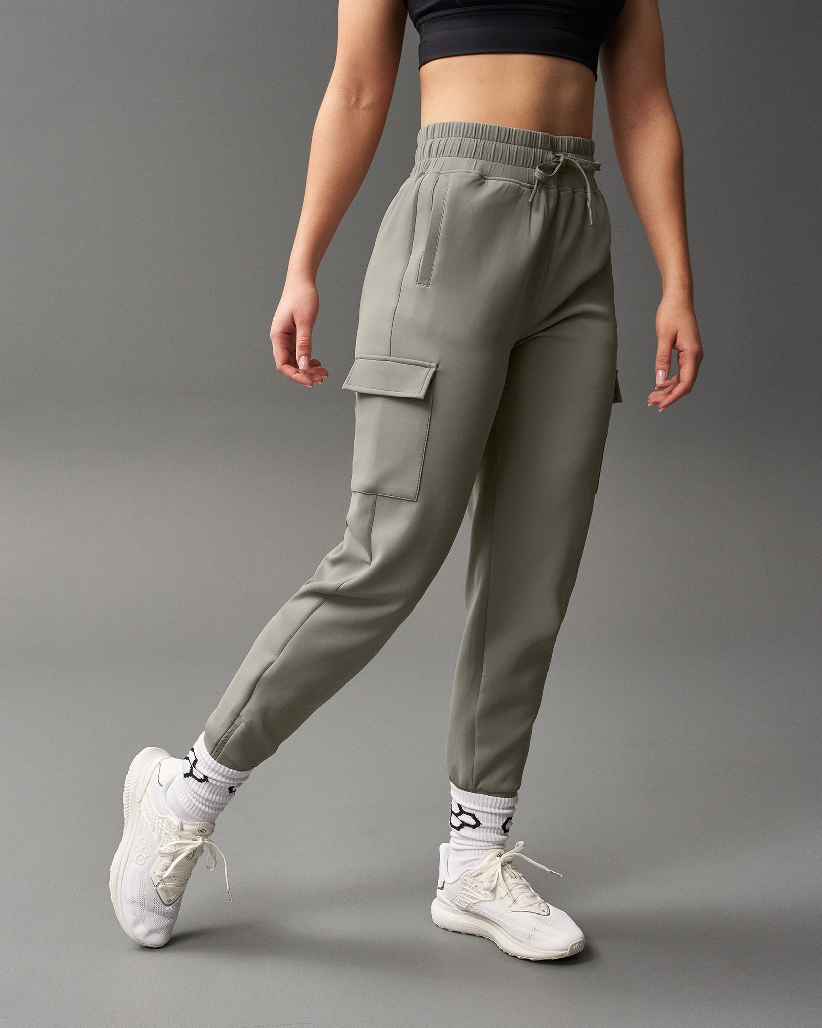 Person wearing olive green cargo jogger pants on a gray background