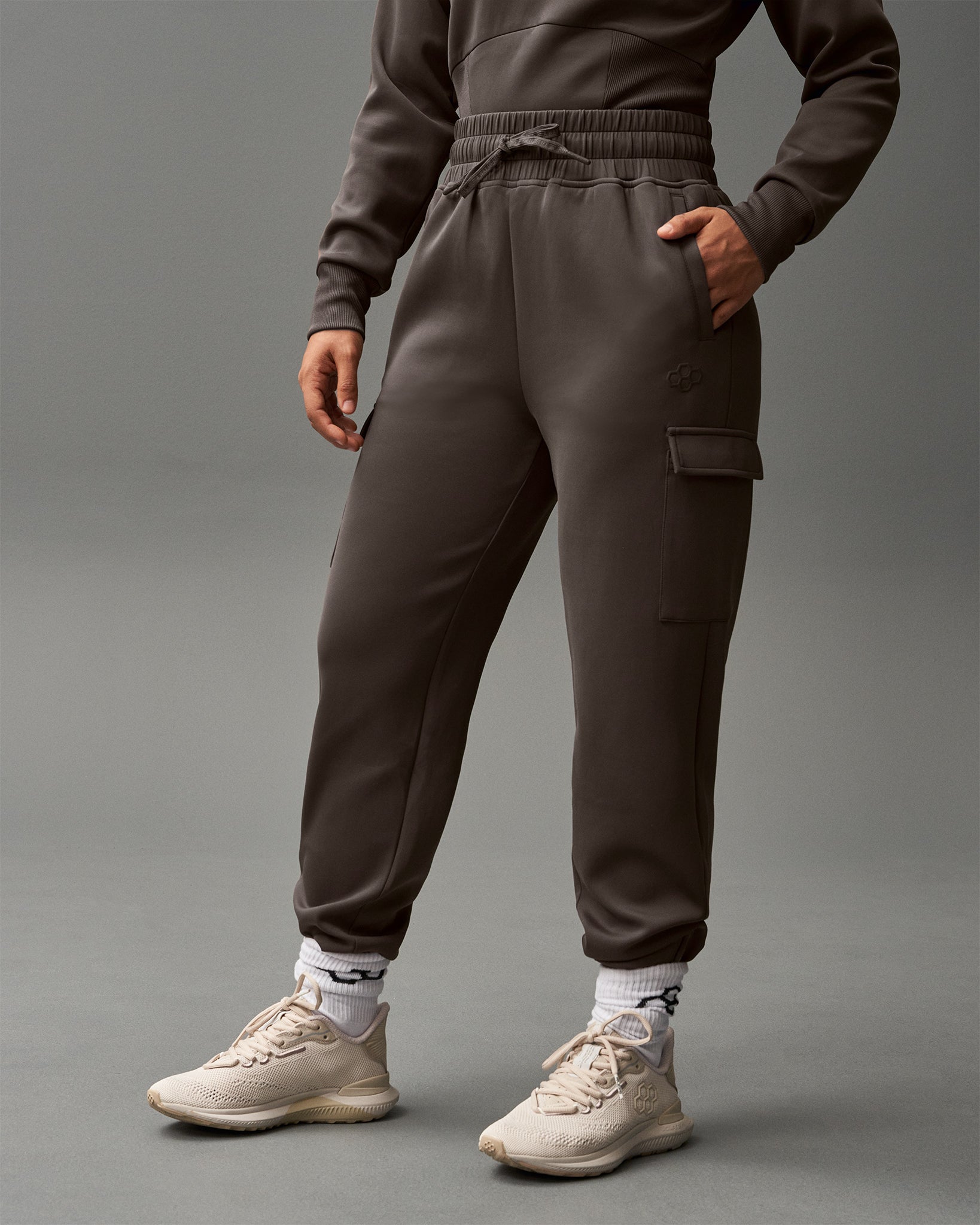 Person wearing a brown tracksuit with beige sneakers on a gray background