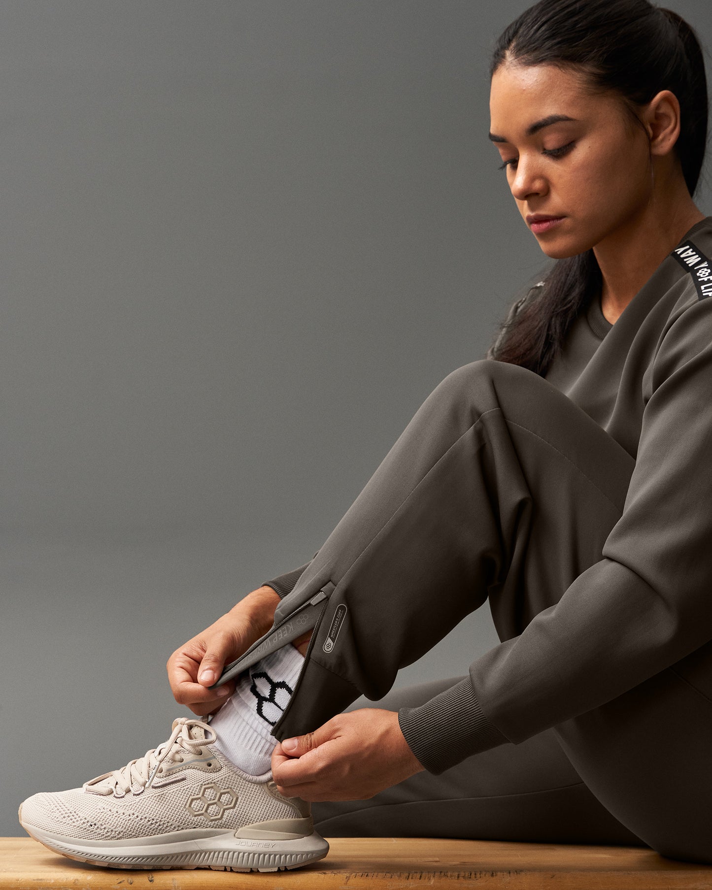 Person tying shoelaces on a white sneaker against a gray background