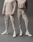 Two people wearing matching light gray outfits on a dark gray background