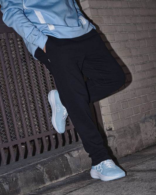 Person wearing a light blue jacket and black pants sitting on a ledge with a brick wall background.