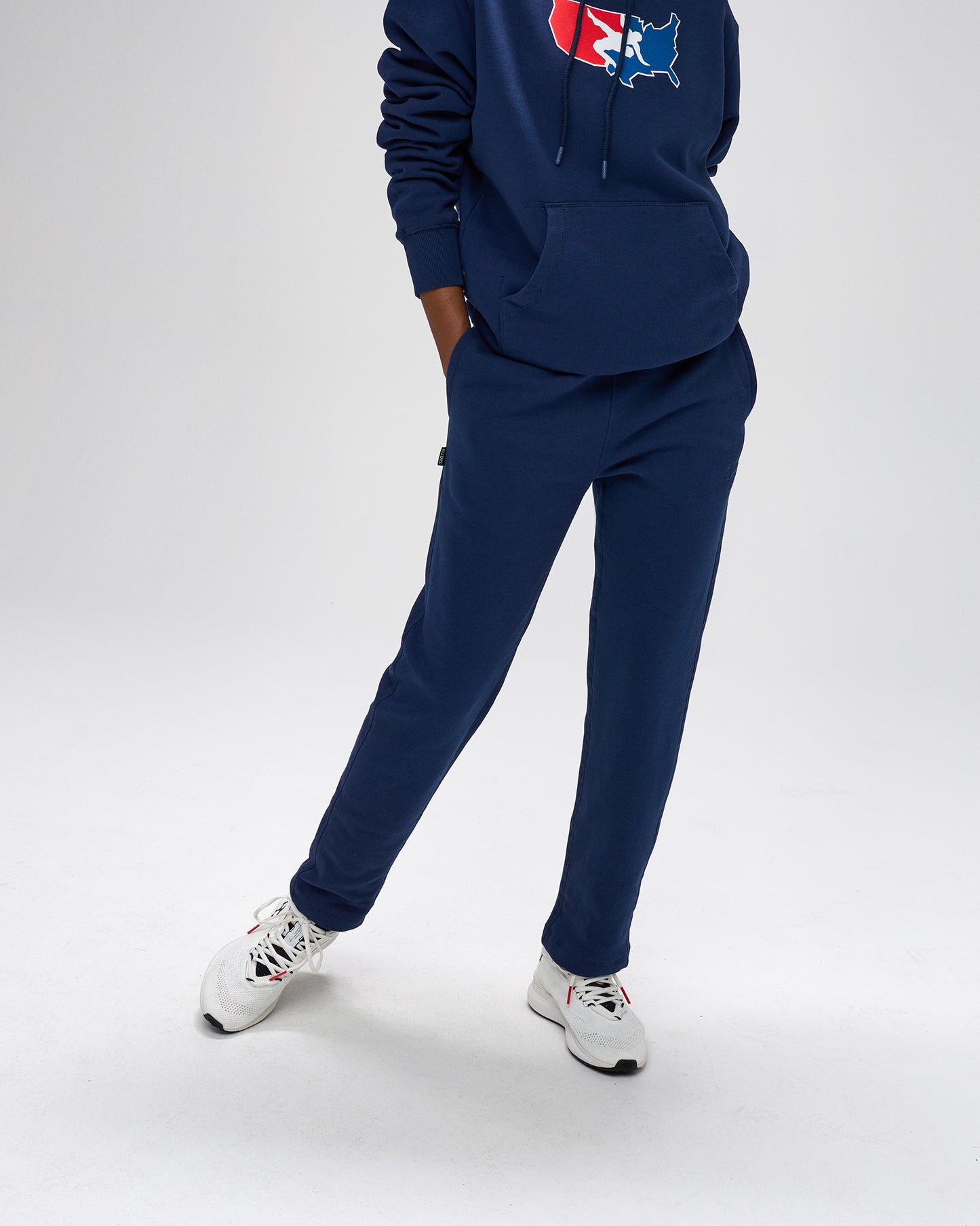 Person wearing a navy tracksuit with a logo on the hood against a white background