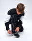 Model adjusting the ankle hem of black RUDIS Movement Podium Pants, highlighting the white piping and adjustable drawcord.