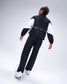 Rear view of model wearing black RUDIS Movement Podium Pants with white piping and matching RUDIS podium jacket.