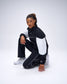 Model wearing black RUDIS Movement Podium Pants in a kneeling pose, showcasing the relaxed athletic fit and white piping details.