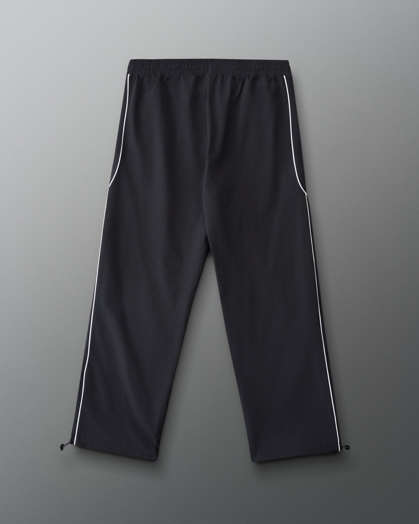 Back view of RUDIS Movement Podium Pants in black with white side piping, relaxed-leg silhouette, and adjustable ankle hems.