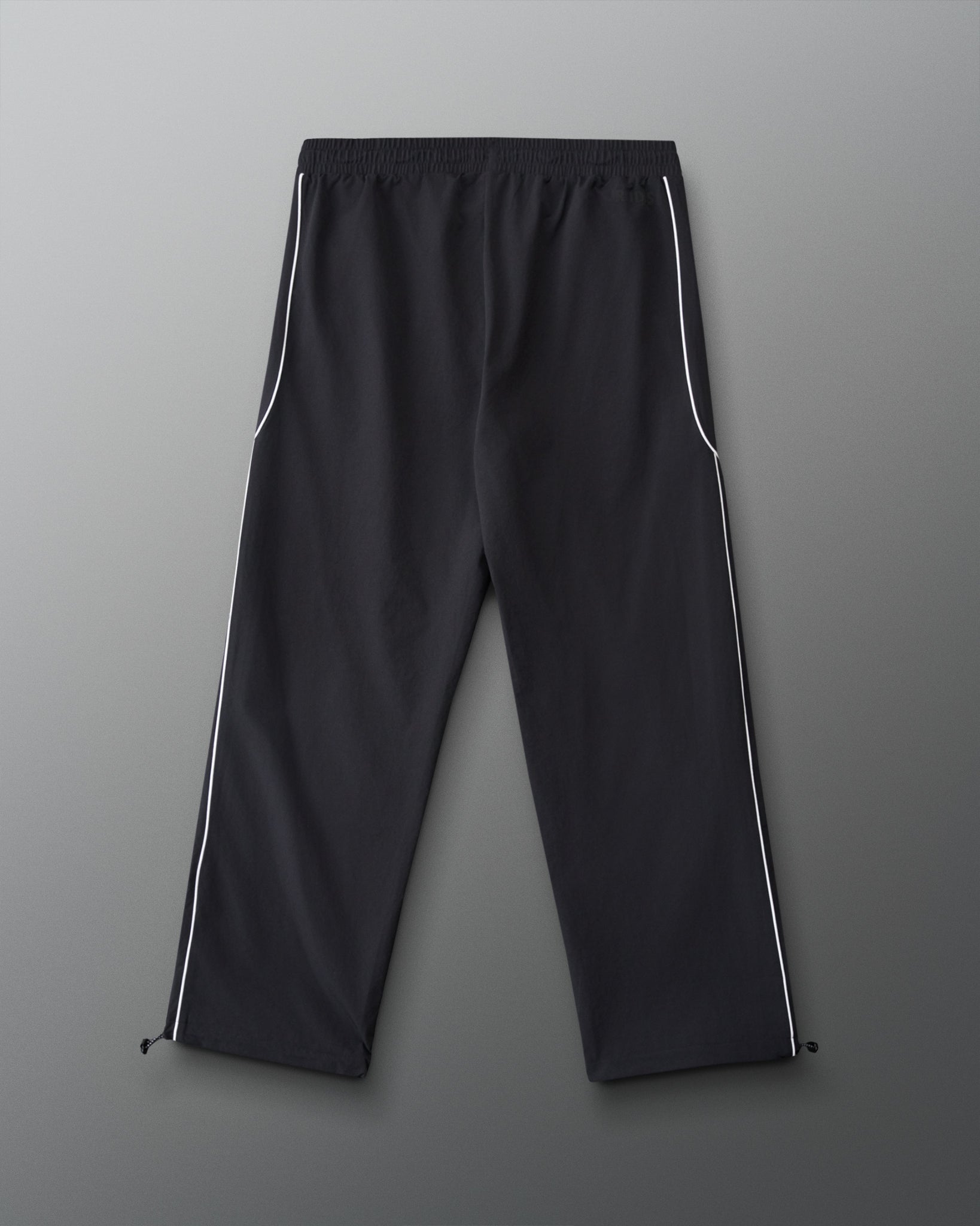 Back view of RUDIS Movement Podium Pants in black with white side piping, relaxed-leg silhouette, and adjustable ankle hems.