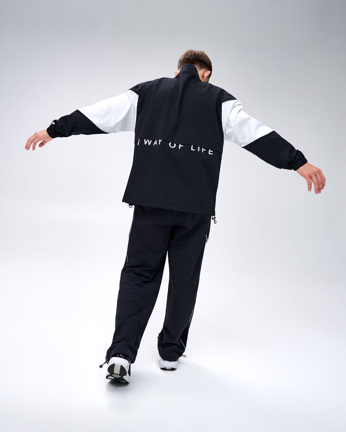 Rear view of model wearing the black RUDIS Full-Zip Movement Podium Jacket and matching pants, showcasing A Way of Life back detailing.