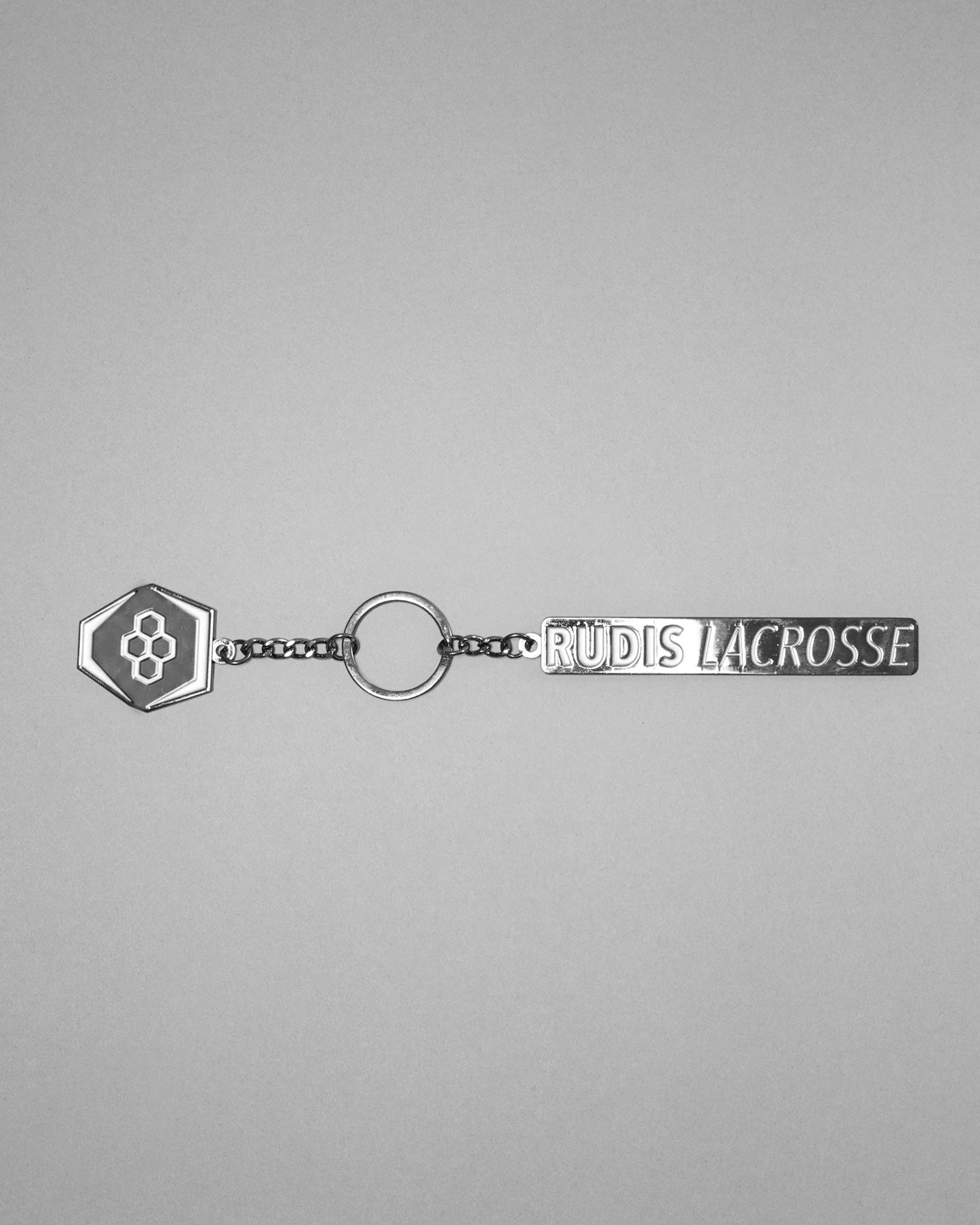 RUDIS Lacrosse metal keychain in black and silver featuring the signature RUDIS hex logo, engraved RUDIS Lacrosse branding, durable metal construction, and split key ring.