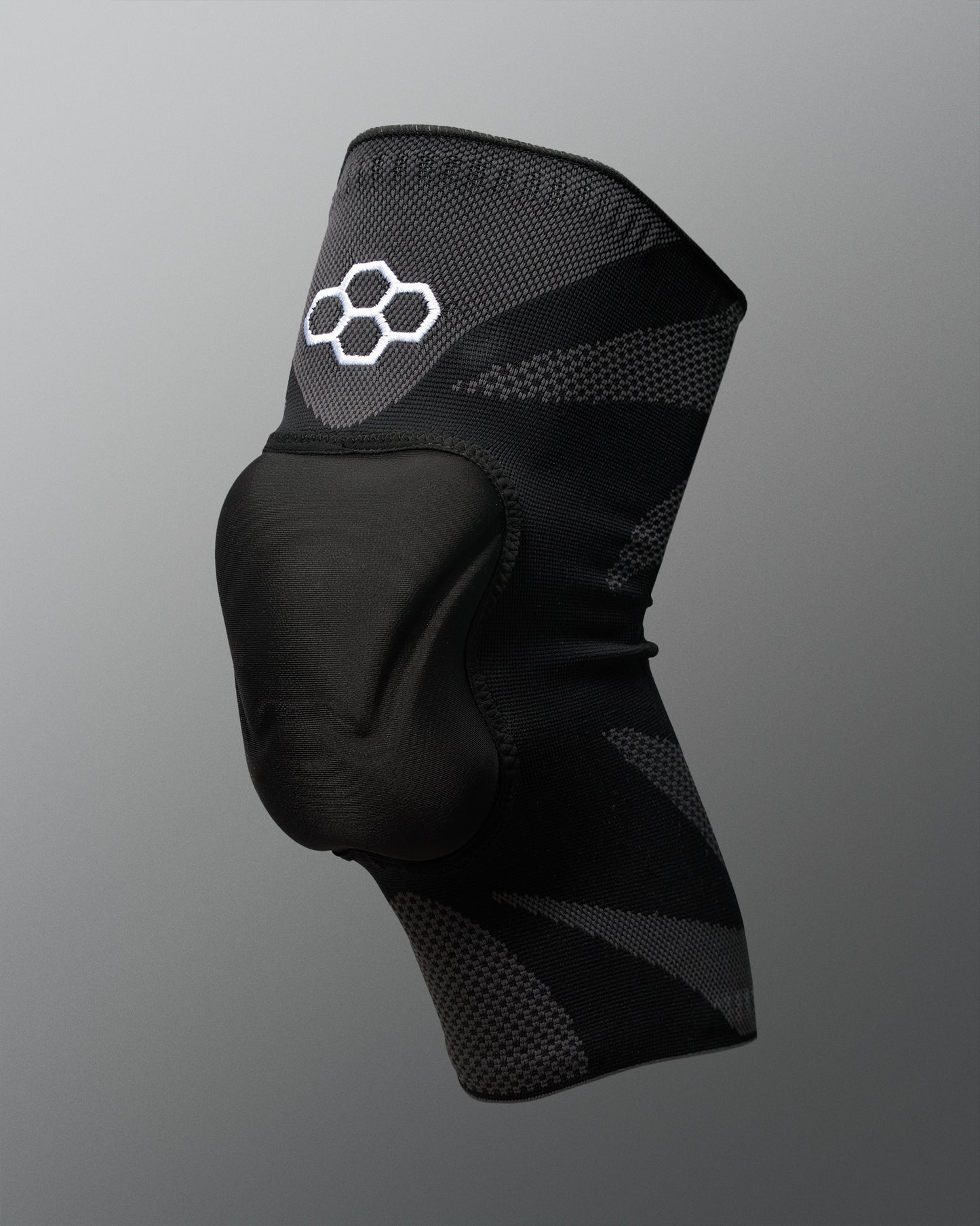 A black knee support brace with a white Quadhex logo on the upper section, set against a neutral gray background.