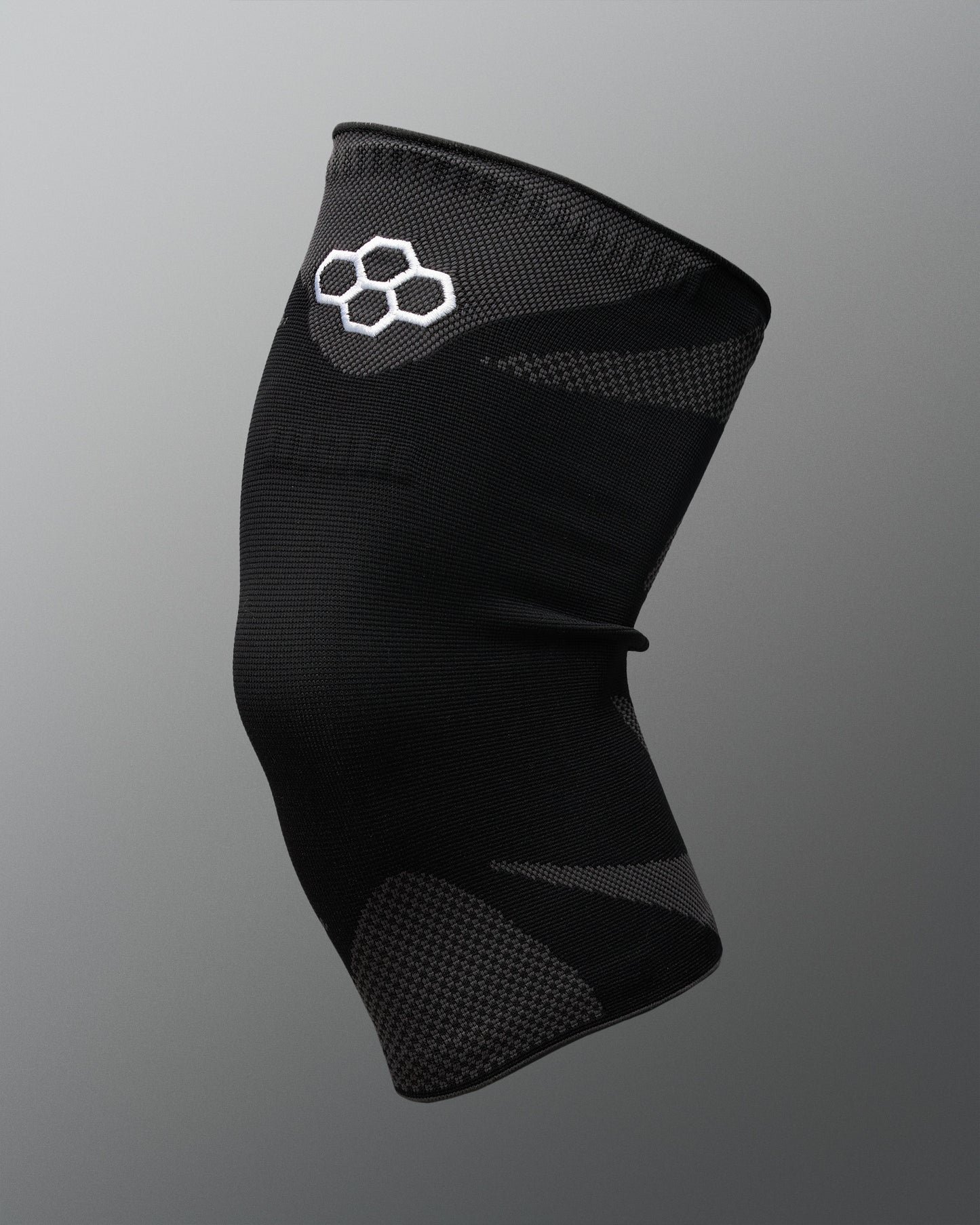 A black athletic knee sleeve with a white Quadhex logo on the upper section, displayed against a neutral gray gradient background.