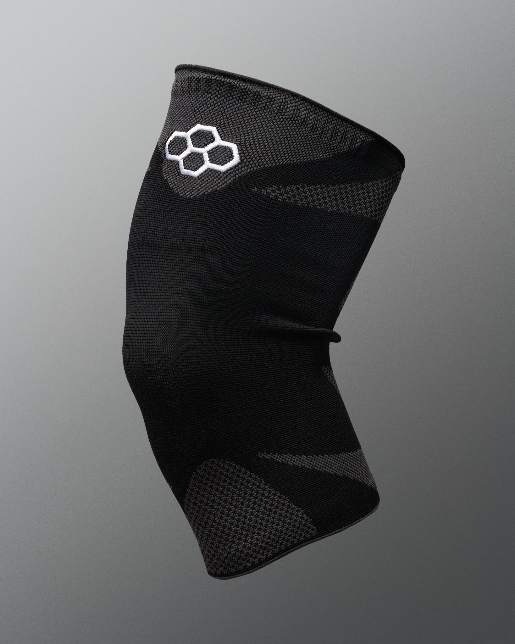 A black athletic knee sleeve with a white Quadhex logo on the upper section, displayed against a neutral gray gradient background.