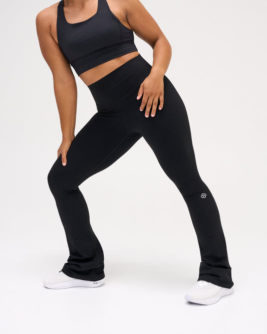 Model wearing black RUDIS Flare Leggings with a high-rise waistband, fitted silhouette, flared legs, and RUDIS knee logo.