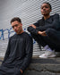 Two people wearing black sweatshirts with visible branding against a metal shutter background.
