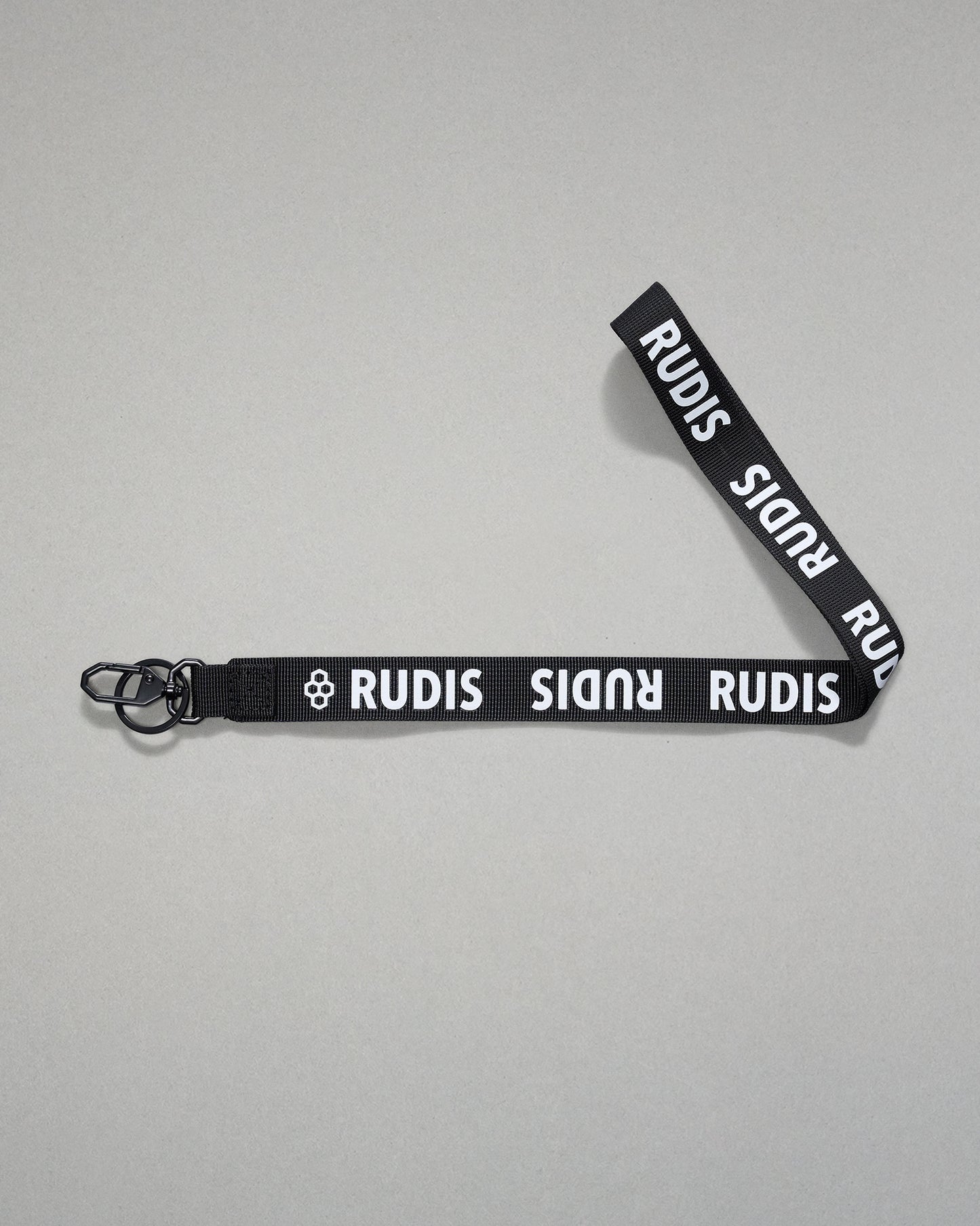 Black RUDIS Wordmark lanyard with repeating white RUDIS logos, woven polyester strap, metal key clip, and key ring for carrying keys, badges, or accessories.