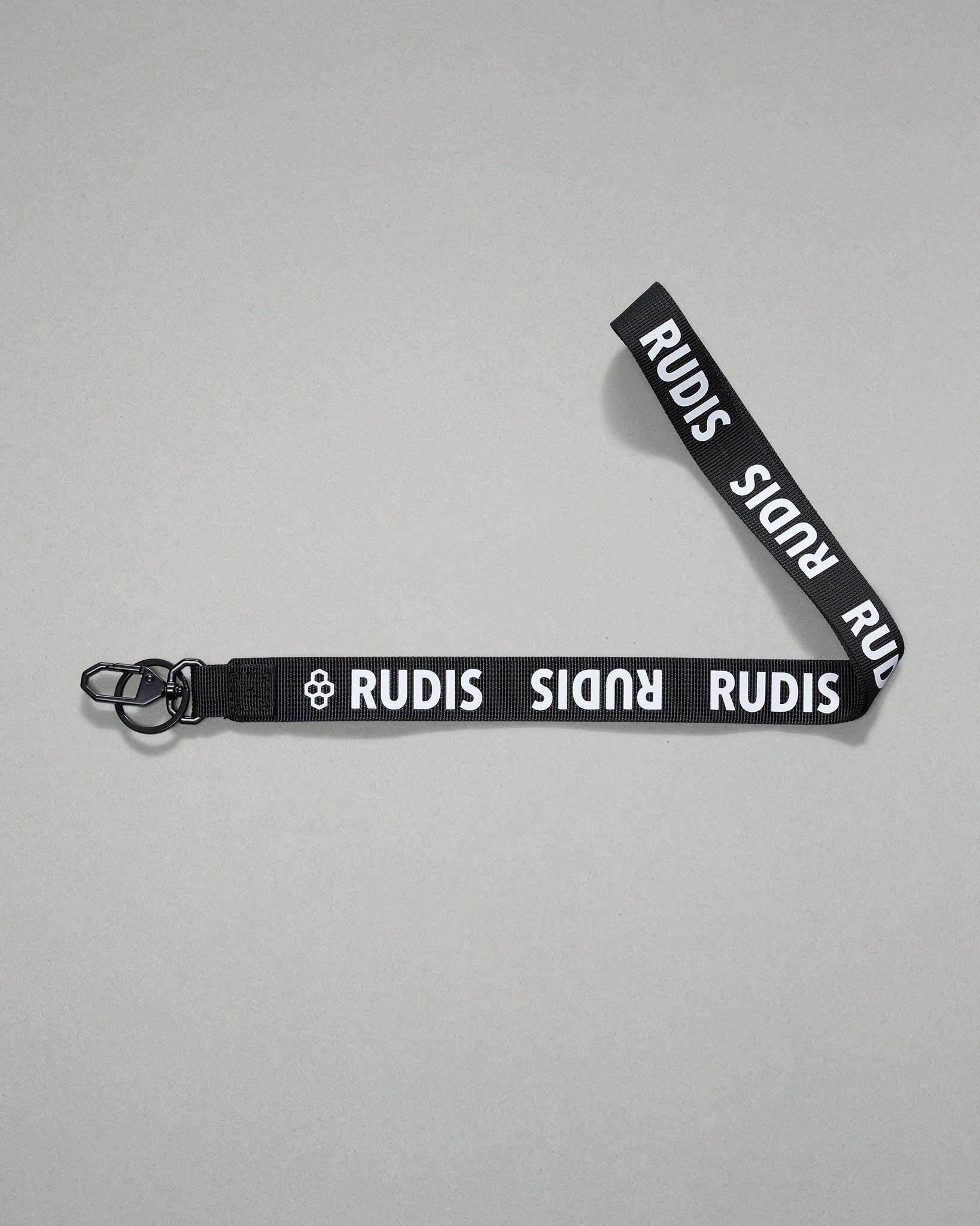 Black RUDIS Wordmark lanyard with repeating white RUDIS logos, woven polyester strap, metal key clip, and key ring for carrying keys, badges, or accessories.