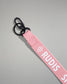 Close-up of the light pink RUDIS Wordmark lanyard featuring a durable metal key clip, key ring, woven polyester strap, and bold white RUDIS logo with honeycomb icon.
