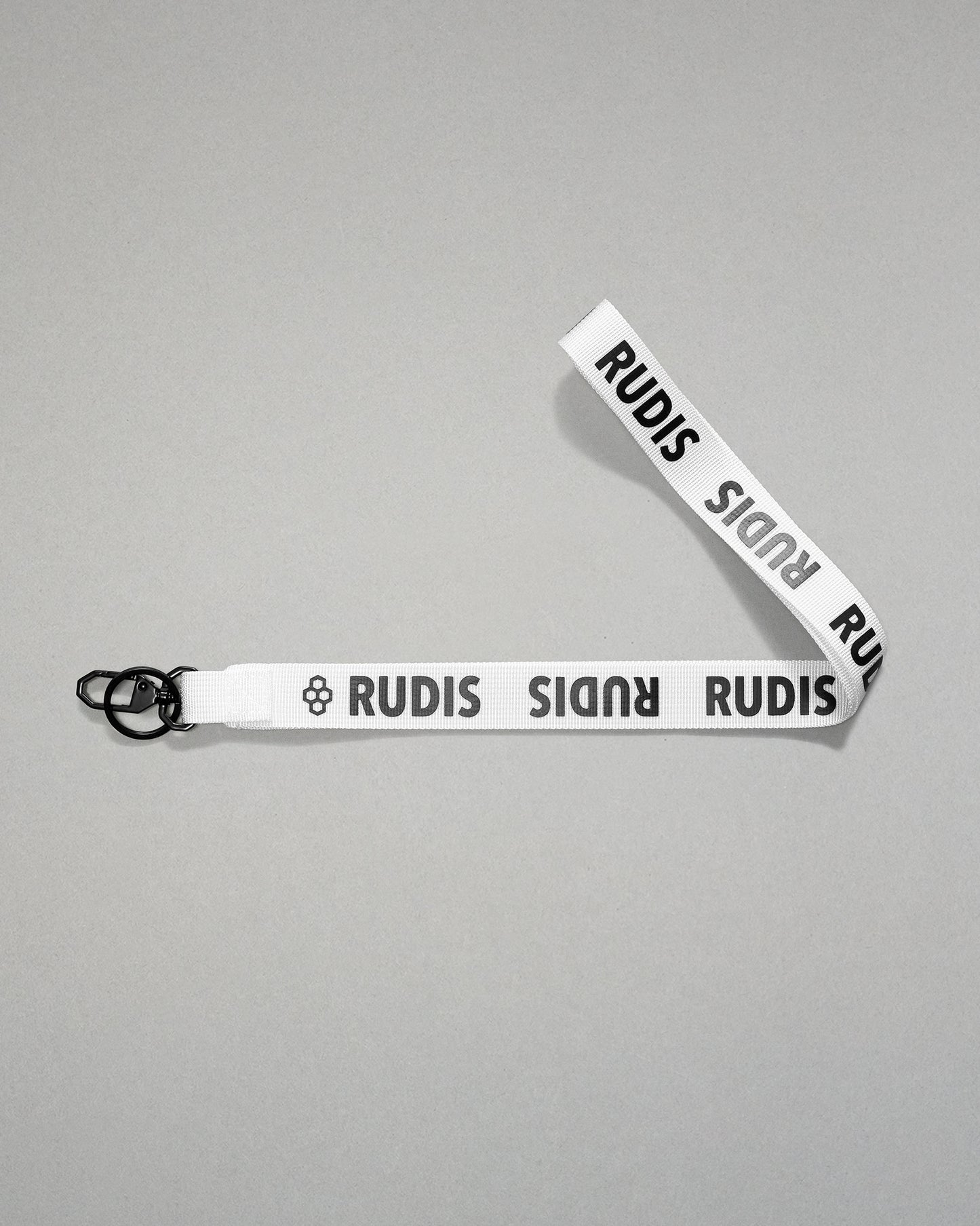 white RUDIS Wordmark lanyard with repeating white RUDIS logos, woven polyester strap, metal key clip, and key ring for carrying keys, badges, or accessories.