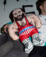 Person holding a wrestling pillow of a muscular figure with a beard, wearing a red wrestling singlet.