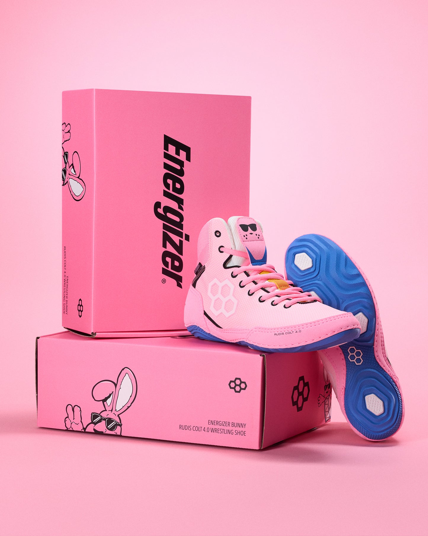 Pink wrestling shoes with blue soles on pink boxes featuring the Energizer logo against a pink background