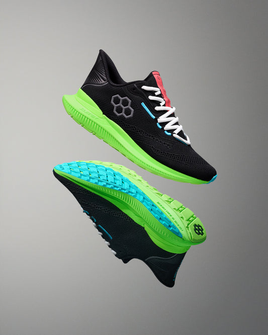 Black running shoes with green and blue soles on a gray background